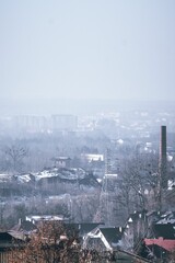 Aerial view over a foggy village with houses and trees under gray misty sky