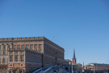 Facades of the royal castle and roof with the royal Swedish flag, the government house and a church tower, a sunny spring day in Stockholm