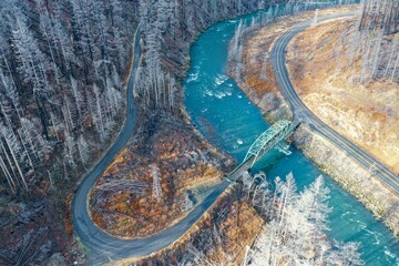 Aerial shot of the bridge over the river connecting the highways between the snowy forest trees