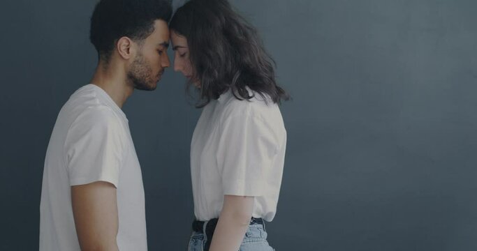 Slow motion portrait of African American guy and Caucasian girl touching foreheads expressing love on gray background. Couple and relations concept.