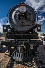 Vertical shot of an old black steam locomotive on the railway against the blue sunny sky