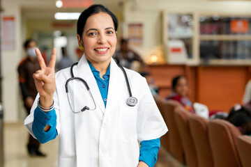 Indian female doctor showing victory sign at hospital.