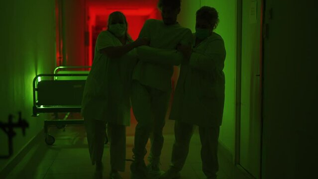A two paramedic are leading a mad ill male patient in straitjacket down corridor in mental hospital. Crazy person with bipolar or psychic disorders. Concept of paranoia or schizophrenia and madness.