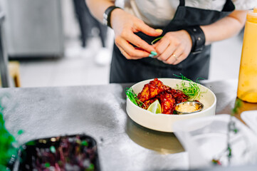 woman chef cooking chicken wings in a sauce in the kitchen