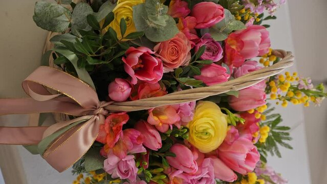 Close-up: woman collects beautiful flower basket. A professional assembles flower arrangement with mimosa and tulip. Woman adjusting flowers in a basket. Vertical video.
