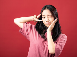 A portrait of a young Indonesian (Asian) woman wearing a pink shirt, making a V sign with her hand. Isolated with a red background