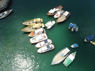 Aerial view of several moored boats on the water near a shore and a pier on a sunny day