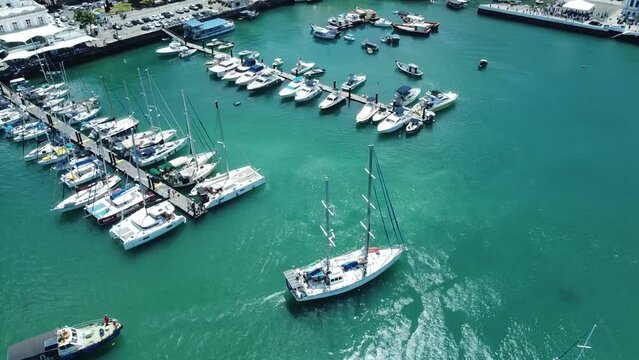 Aerial view of several moored boats on the water near a shore and a pier on a sunny day