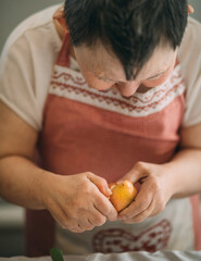 Lifestyle, education. An elderly woman with down syndrome is studying in the kitchen peel the...