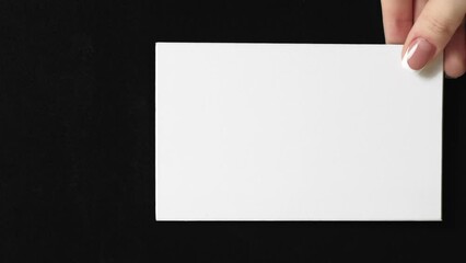 Vertical video. Mockup letter. Advertising card. Female hand showing blank white paper with empty space on black background loop. - Powered by Adobe