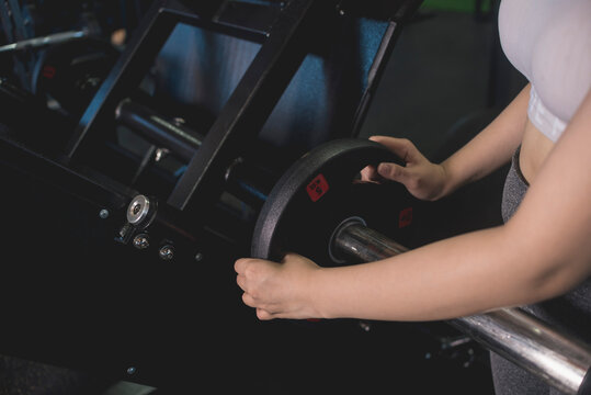 A young anonymous woman loading plates for more weight on a leg press machine at the gym.