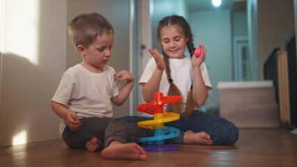 Fototapeta premium children baby play together toys in kindergarten. happy family preschool education indoor concept. baby boy and girl play toy roll a ball down a slide on lifestyle the floor rejoice in kindergarten