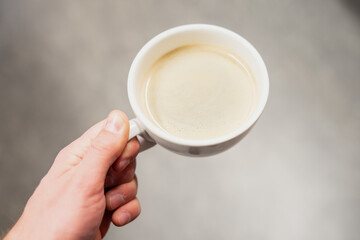 Man holding white coffee in white mug in the morning with grey floor background