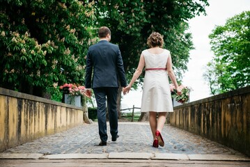 Fototapeta premium Back view of the bride and the groom walking in a park