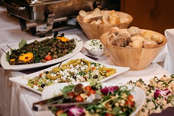 Closeup of dishes on white plates and bread on wooden bowls in white tablecloth