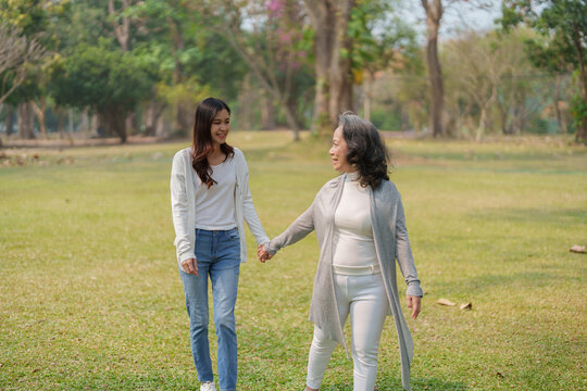 Adult daughter holding her elderly mother hand with love and walk together in park