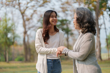 Fototapeta premium Adult daughter holding her elderly mother hand with love and walk together in park