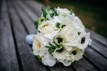 Closeup shot of the bridal white flowers bouquet on a wooden bench in the park with blur background