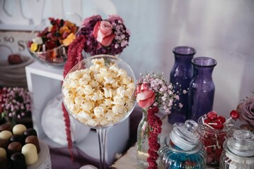 Closeup shot of the popcorn in a big glass with chocolate candies in the blur background