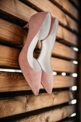 Fototapeta na wymiar Closeup shot of the pink shoes of the bridesmaid hanging on a wooden planks wall