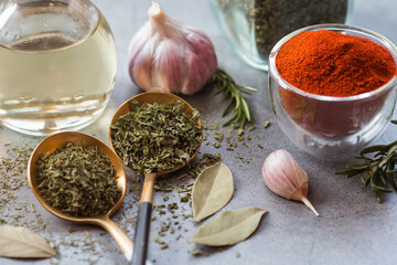Fragrant spices. Dried parsley, dill, paprika, rosemary, garlic, bay leaf and a bottle of oil on a gray background. Free space.