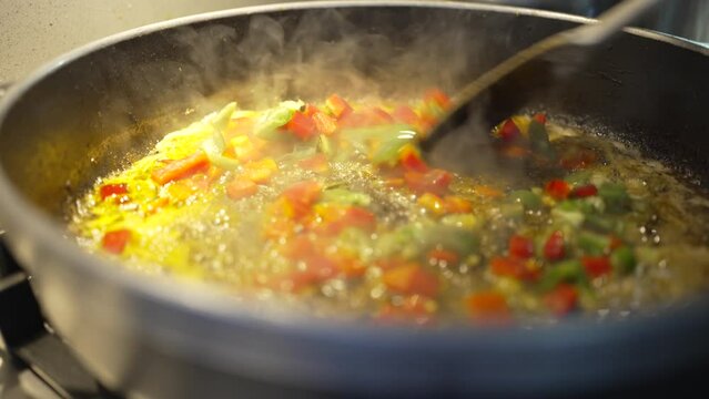 hand detail video of older father cooking, throwing red and green pepper into paella to make sofrito, hot olive oil