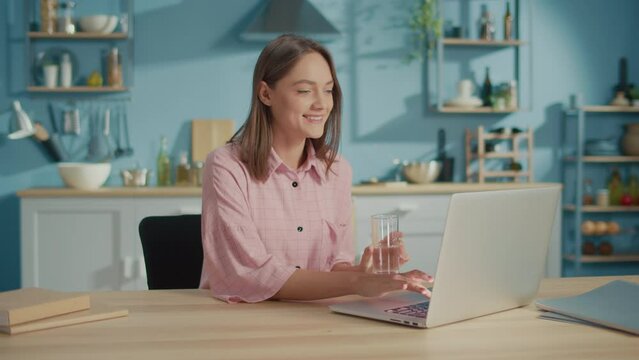 Freelance Young Woman Drink a Glass of Clean Water in Kitchen. Smiling Woman Start New Day with Healthy Life Habit, Holding Glass Drinking Clean Mineral Natural Water. Lifestyle Healthcare Concept.