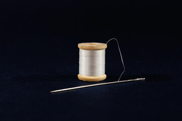 Studio shot of a white thread reel and a sewing needle isolated on a black background. Spool (or...