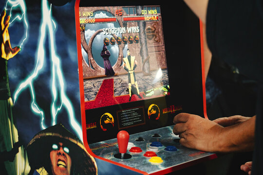 Close-up of an old retro gaming arcade game - Mortal Kombat II, with a man's hands on the cabinet control panel