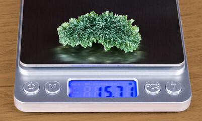 Closeup of beautiful green moldavite gemstone on weighing scale with digital display. Accurate...