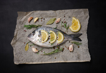 Raw whole dorado fish on brown parchment paper and spices for cooking, top view on black table