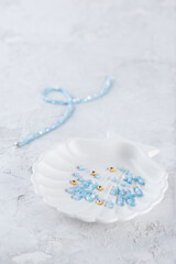 Blue mother-of-pearl and gold beads on a tray with a choker on a light background, jewelry making.