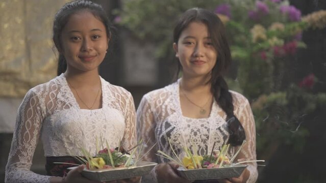 Two Beautiful Balinese Women Girls with Traditional Outfits Smiling Holding Canang Sari Daily Offerings