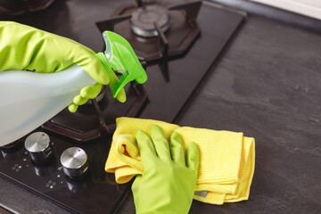Woman's Hand in Green Glove Splashes Eco Detergent to Gas Cooker. Closeup of Glass Stove Top.