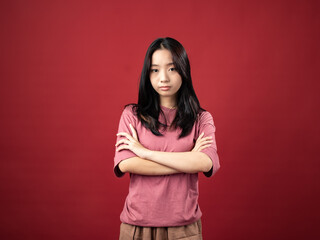 A portrait of a young Indonesian (Asian) woman wearing a pink shirt, posing with folded hands. Isolated with a red background