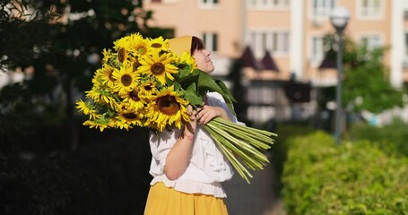 Huge bouquet of fresh sunflowers in hands of a smiling women in yellow skirt outdoor. Patriotic gift with love, gratitude. Mothers Day. Support for Ukraine. Independence Day. High quality 4k video - Powered by Adobe