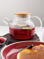 tea with lemon in a teapot with cheesecake and berries
