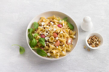 Italian pasta campanelle with radishes, feta cheese, walnuts and arugula in a white plate on a light gray background