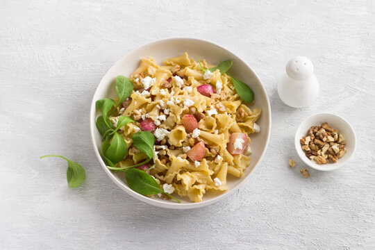 Italian pasta campanelle with radishes, feta cheese, walnuts and arugula in a white plate on a light gray background