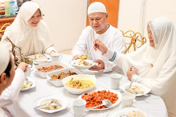 Obraz na płótnie Canvas Family togetherness at eid mubarak moment. Mother serving ketupat lebaran and chicken curry soup at dining room. 