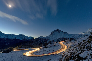 Lights of car trails on winding road covered with snow at night, Bernina Pass, Val Poschiavo, Graubunden canton, Switzerland