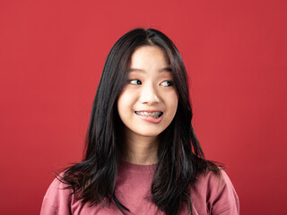 Fototapeta premium A close-up portrait of a young Indonesian (Asian) woman wearing a pink shirt. Isolated with a red background