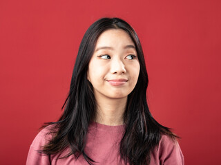 Fototapeta premium A close-up portrait of a young Indonesian (Asian) woman wearing a pink shirt. Isolated with a red background