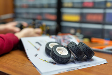 Focus on four wheels of constructor laying on building plan on the table. Playing with modern constructor