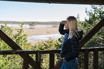 A beautiful young girl looks into the distance on an observation tower in a swamp in Estonia.