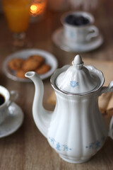 Cup of tea or coffee, plate of cookies, cup of blueberries, plate of chocolate, glass of juice, book, reading glasses, teapot, flowers and lit candles on the table. Brunch or afternoon tea concept.