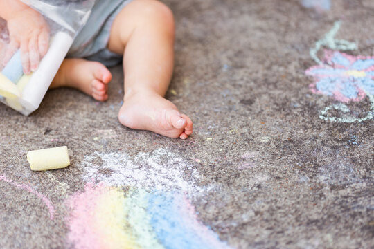 chalk covered foot of baby on concrete with rainbow art drawing