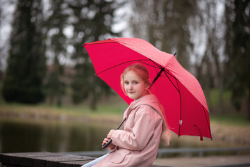 a girl under a red umbrella sits near the lake. walks in the open air