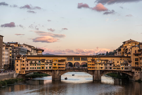View of a gondola boat sailing the Arno River at sunset with Ponte Vecchio bridge in background, Florence, Tuscany, Italy.