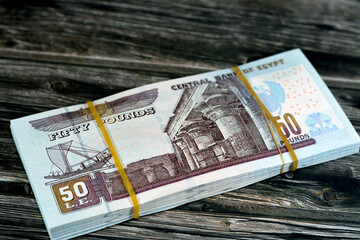 Egypt money stack of pounds isolated on wood background, pile of 50 EGP LE fifty Egyptian pounds cash money bills with a image of Abu Hurayba Mosque, temple of Edfu and winged scarab, selective focus - obrazy, fototapety, plakaty